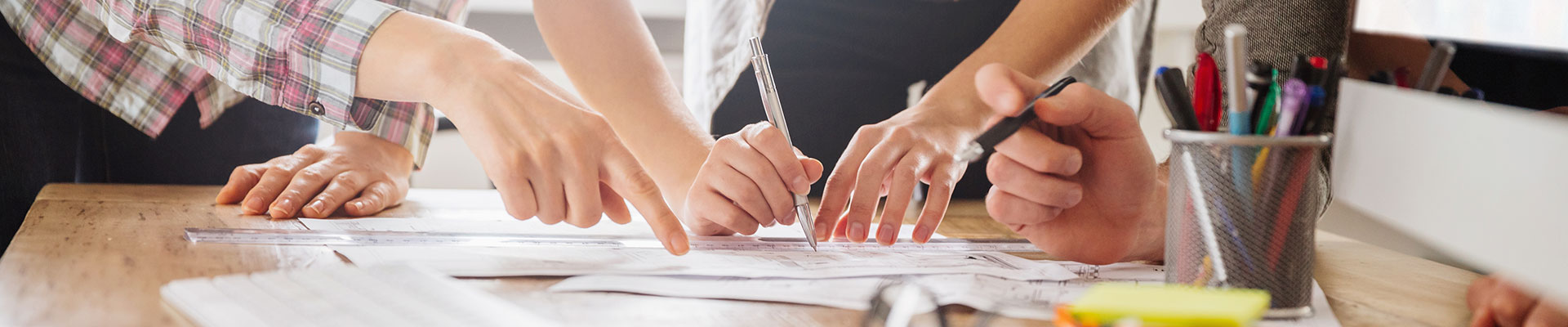 Les mains de trois personnes montrent un ou écrivent sur un papier sur une table.
